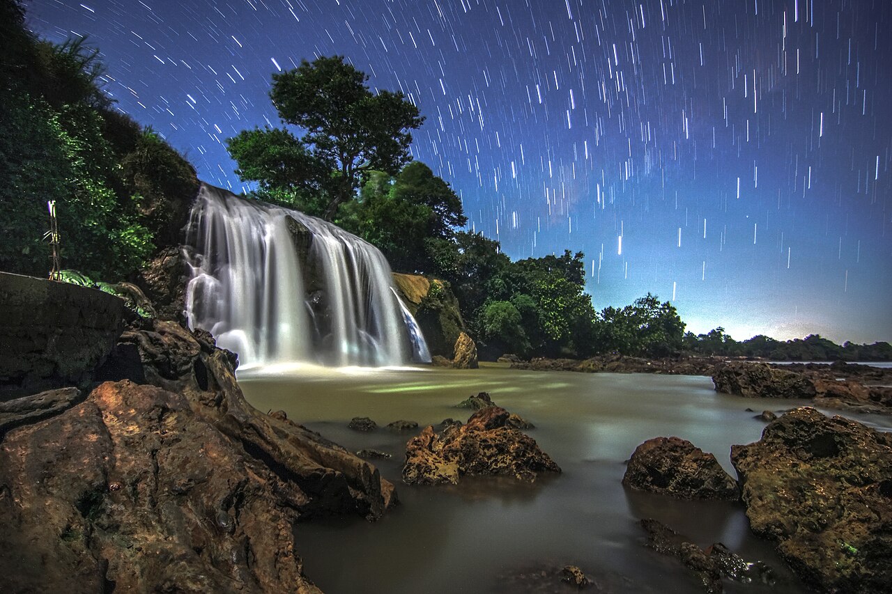 Air Terjun Toroan dipotret malam hari, airnya jatuh ke hamparan batu karang di tepi laut