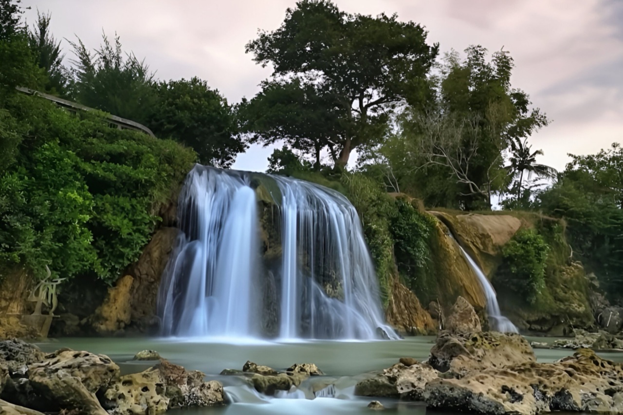 Air Terjun Toroan mengucur dari tebing berlumut ke kolam dangkal berbatu karang di tepi laut