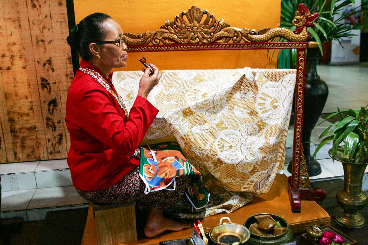 Seorang perempuan duduk membatik kain putih dengan canting