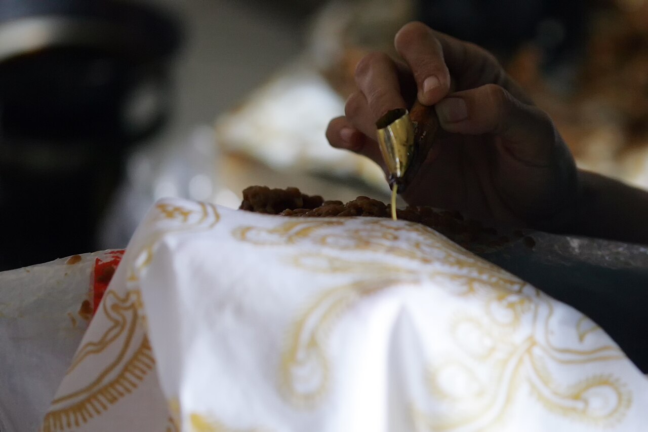 Tangan menorehkan malam panas dari canting ke kain putih yang sudah bermotif