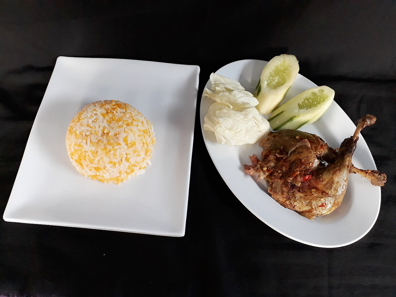 Sepiring bebek songkem dengan nasi jagung, timun, dan kerupuk di sisinya