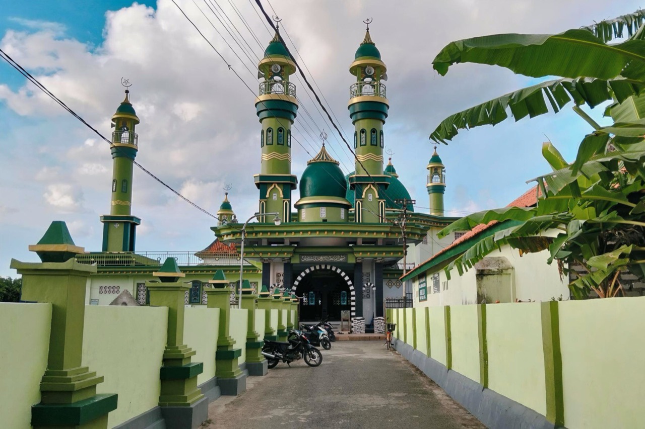 Masjid Madegan dilihat dari jalan kampung, dengan kubah dan menara hijau muncul di balik pagar