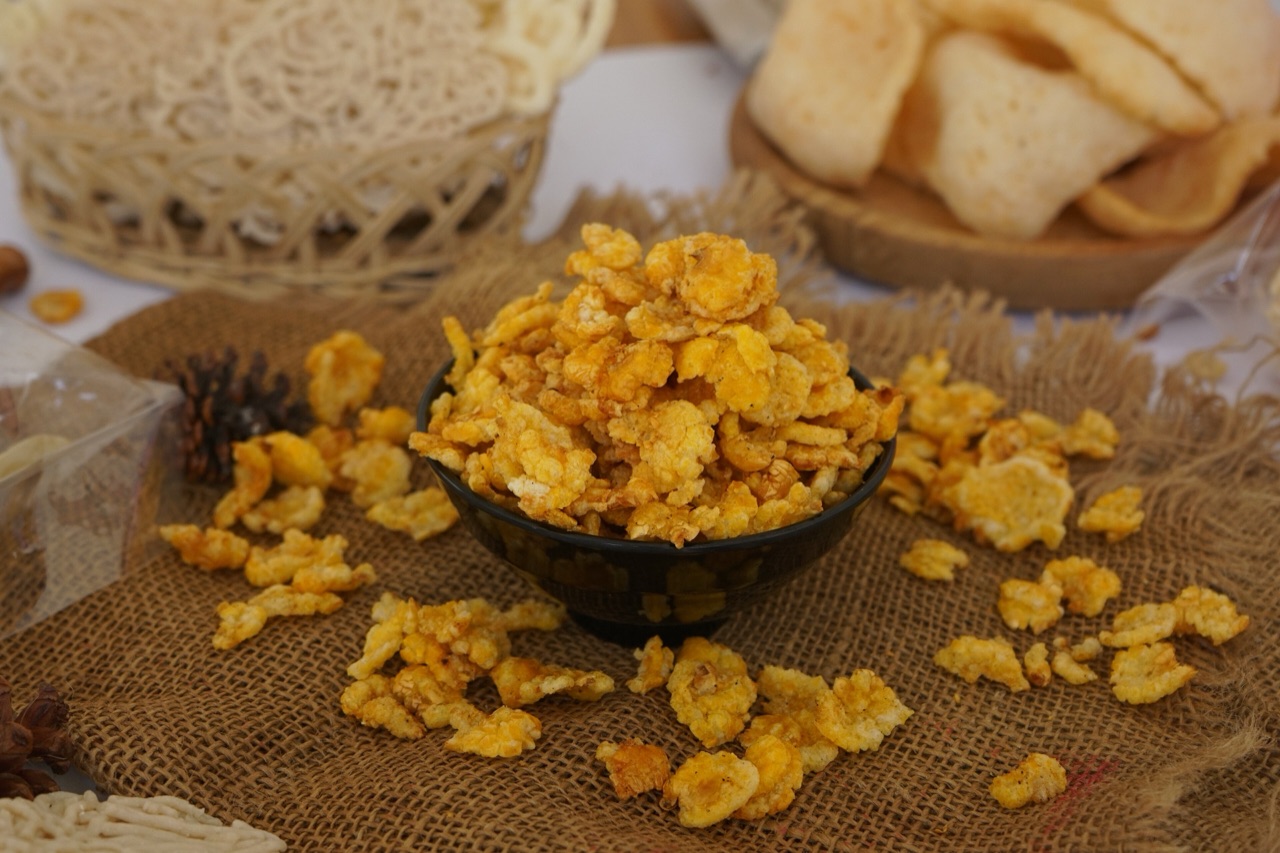 Semangkuk emping jagung berwarna kuning keemasan, sebagian berhamburan di atas kain goni