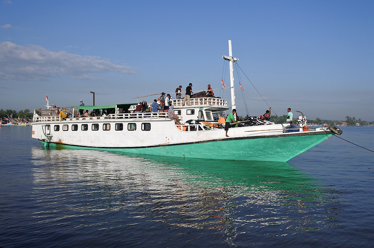 Kapal layar motor berbadan putih dan hijau penuh penumpang di laut