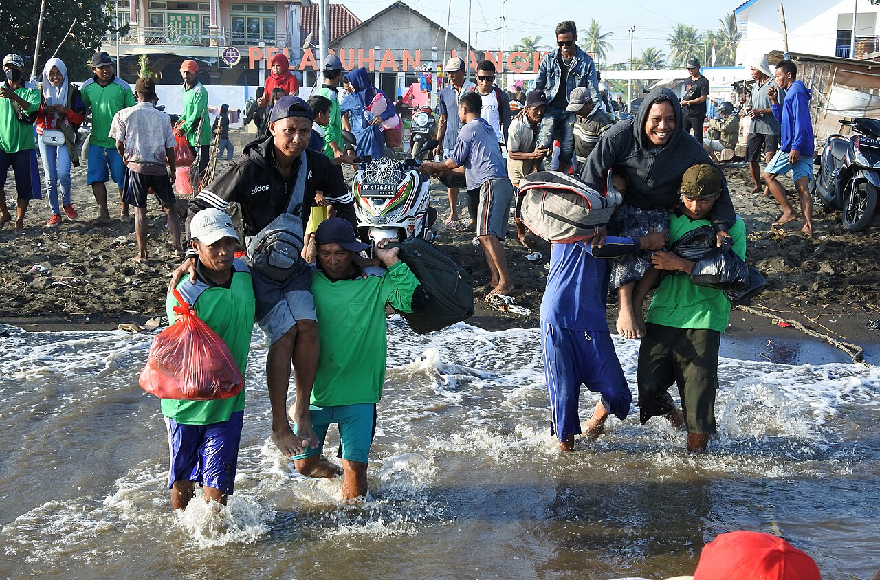 Buruh angkut menggendong penumpang melewati air dangkal menuju perahu