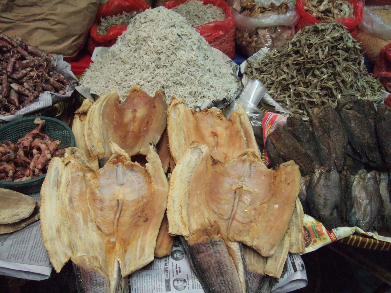 Lapak pasar berisi tumpukan teri nasi putih, teri kering, dan ikan belah yang sudah dikeringkan di atas koran