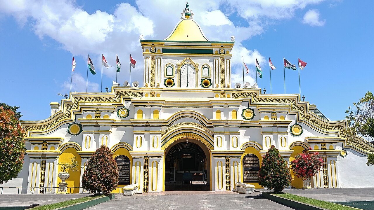 Gapura Masjid Jamik Sumenep berwarna kuning dan putih dengan tiga lengkung dan menara jam