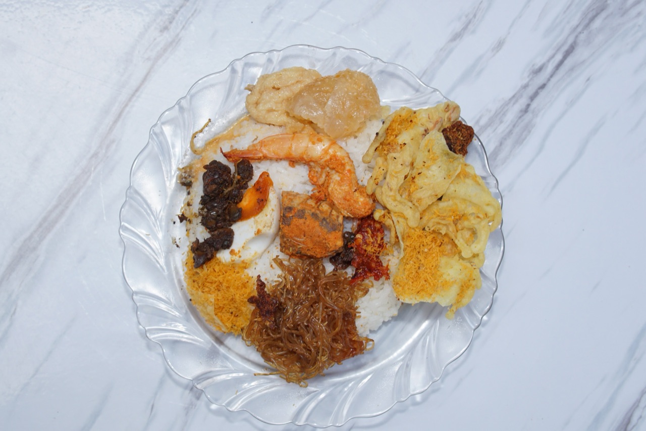 Sepiring nasi serpang di piring kaca berisi nasi putih, udang, soun, serundeng, kerupuk, dan sambal