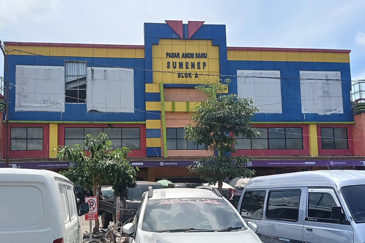 Gedung Pasar Anom Baru blok A bercat biru dan kuning dengan mobil parkir di depannya