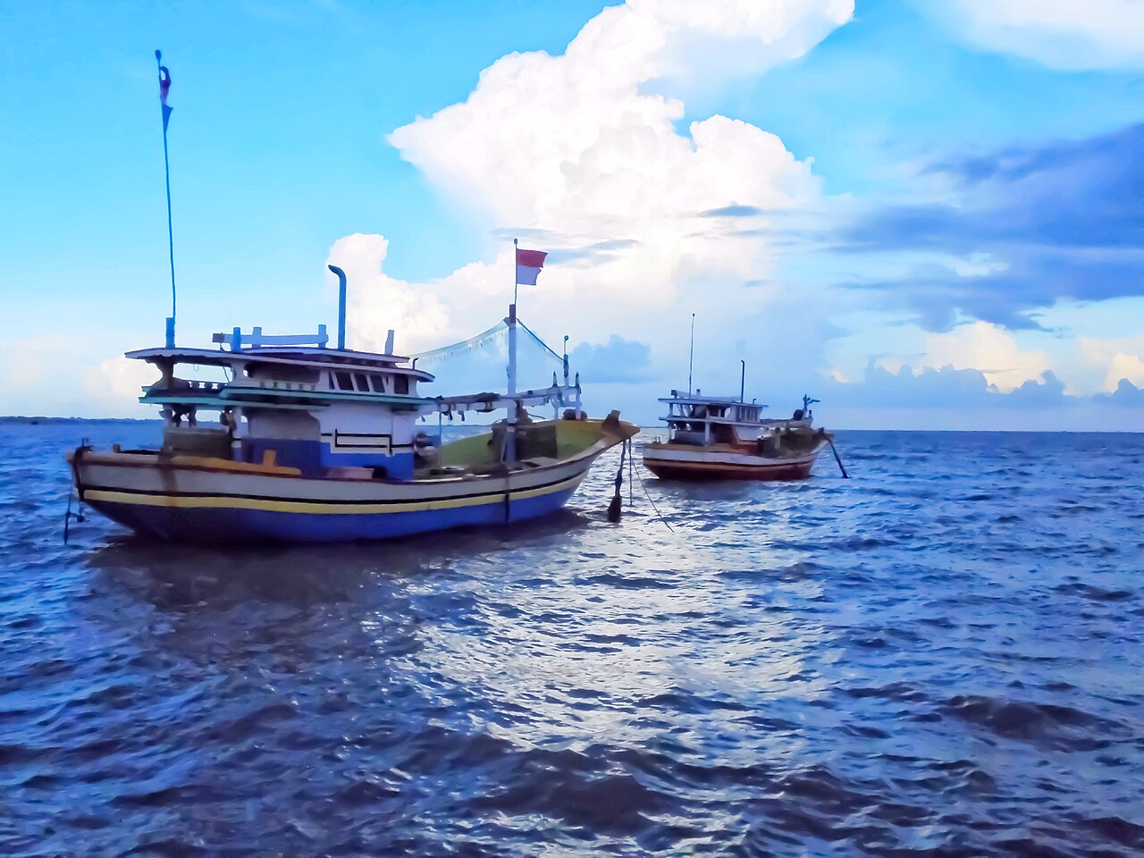 Dua perahu nelayan kayu di laut lepas, satu mengibarkan bendera di tiangnya