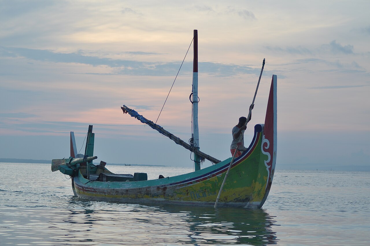 Perahu kayu tradisional Madura berhaluan tinggi di air dangkal menjelang senja