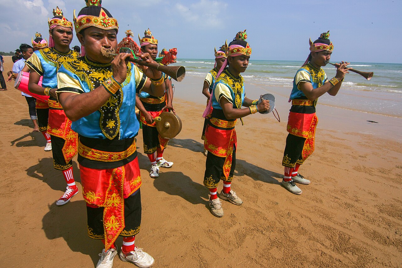 Rombongan pemusik saronen berkostum merah dan biru bermain di tepi pantai