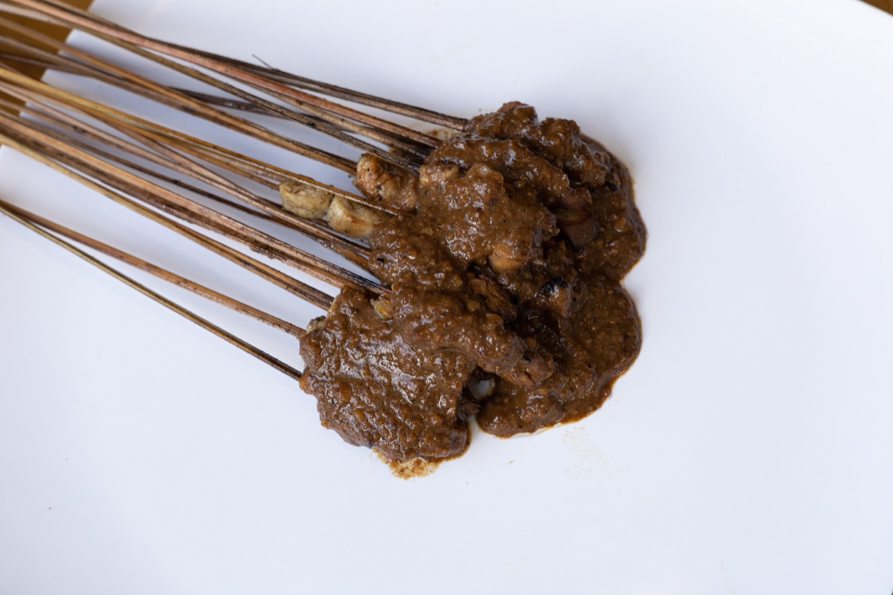 Seikat sate lalat bertusuk lidi tipis berlumur bumbu kacang kental di atas piring putih