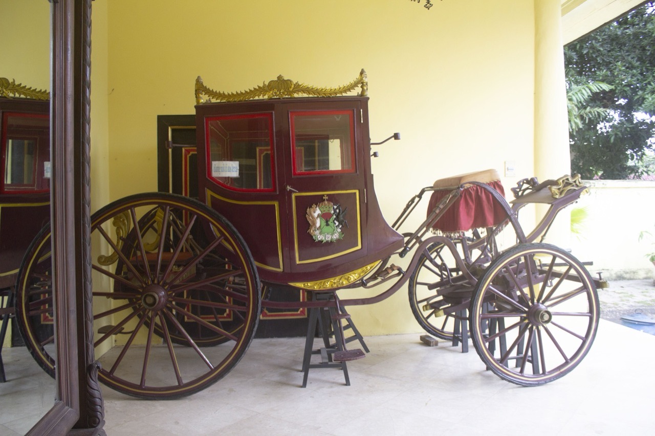 Kereta kencana tua berwarna merah tua dengan ukiran emas dan lambang kerajaan di pintunya