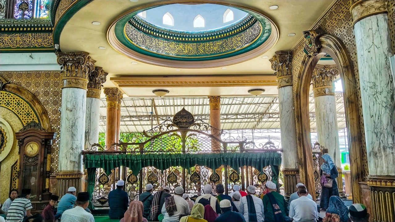 Bagian dalam kompleks makam Syaichona Kholil, peziarah duduk di lantai menghadap cungkup berukir kuning keemasan