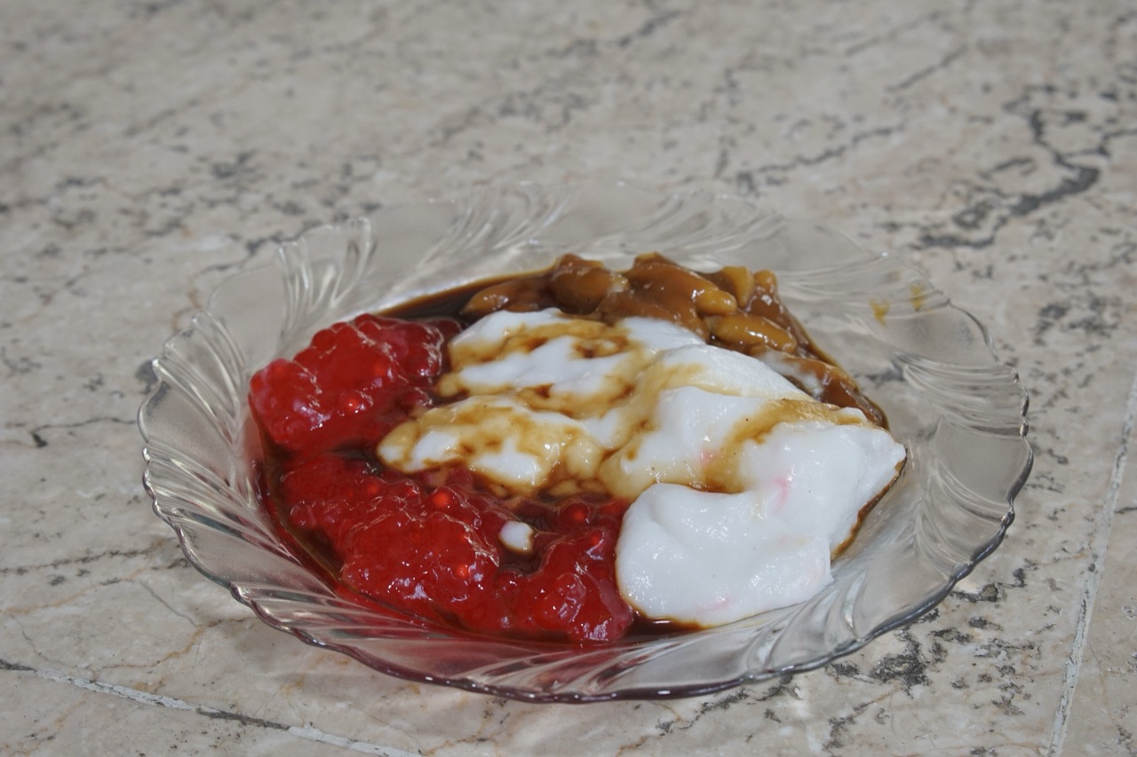 Satu porsi tajin sobih di piring kaca berisi bubur putih, bubur merah, dan bubur cokelat yang disiram gula merah