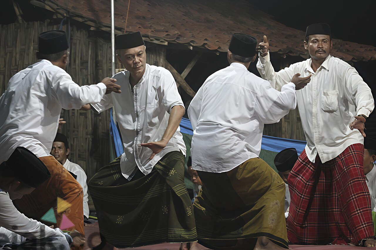 Sekelompok laki-laki berbaju putih dan berkopiah menari sambil membawa alat musik