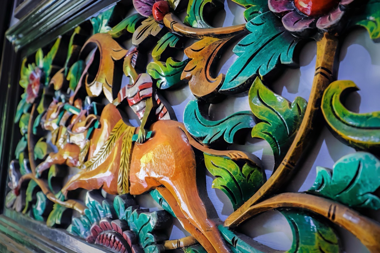 Ukiran kayu berlubang bermotif sulur dan bunga dengan figur hewan berkaki di antaranya, dicat hijau, merah, dan oker
