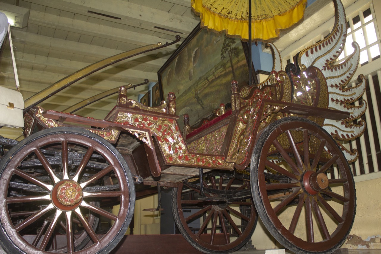Kereta kayu berukir dan berlapis emas dengan roda jeruji besar di dalam ruang museum