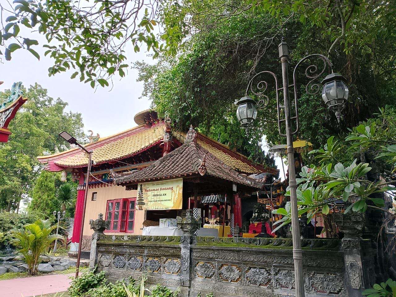 Pura beratap tumpang dengan pagar batu berukir berdiri persis di sebelah bangunan vihara beratap genteng kuning