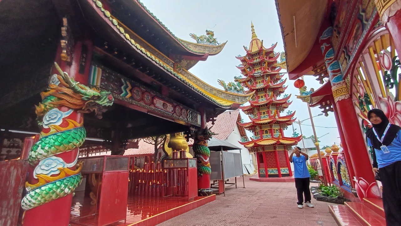 Halaman vihara dengan bangunan merah keemasan berukir naga hijau di kiri dan pagoda merah bertingkat di tengah